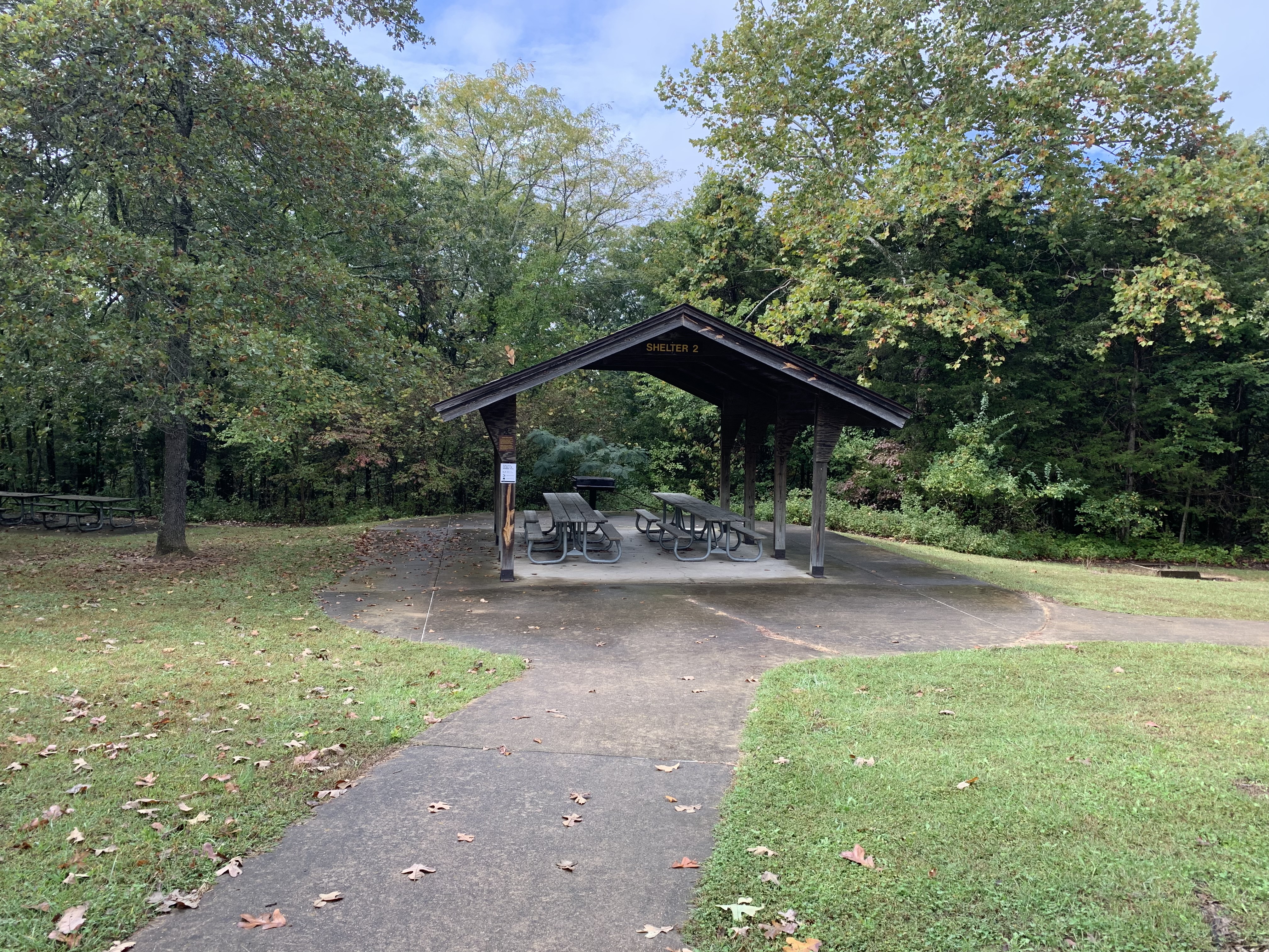 Open picnic table with concrete path leading to it and grill and background