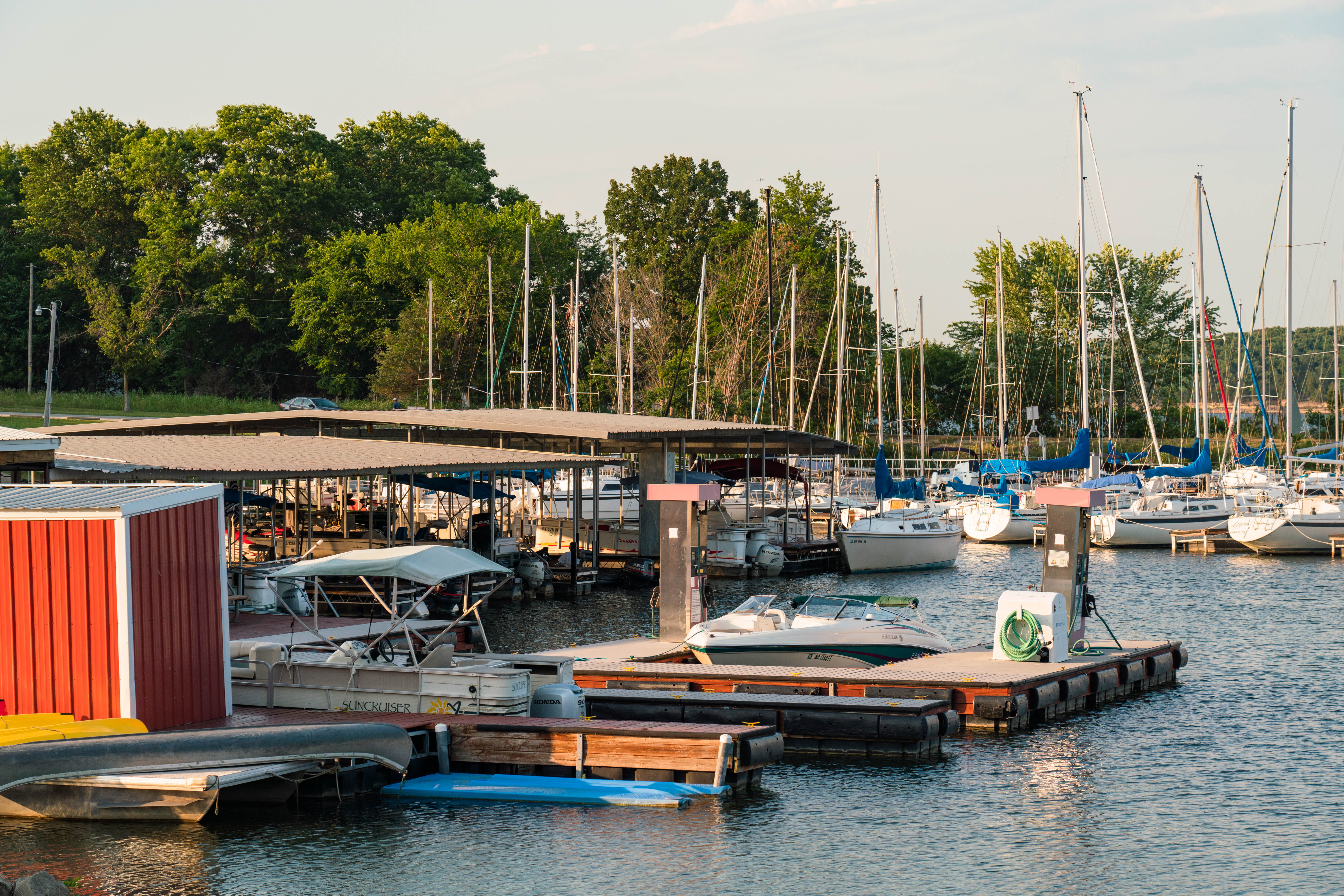 Sailboats, motorized fishing boats, a pontoon boat, a personal watercraft and a canoe docked at the marina boat slips on a sunny day