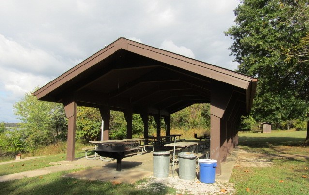 Open picnic shelter with grill and trash cans and recycle bin in foreground
