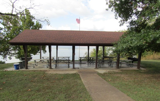 Head-on view of open picnic shelter with trash cans to the left and Stockton Lake in the background