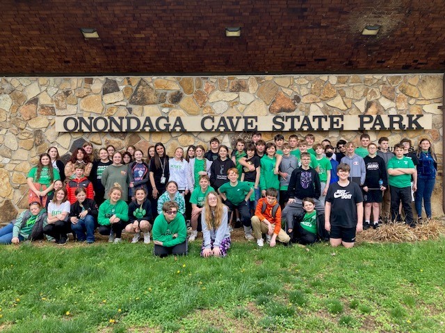 Over 50 students pose in front of a stone wall with "ONONDAGA CAVE STATE PARK" on it