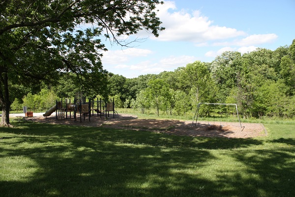 playground equipment with slides and a swing set in a shaded area