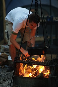 Man taking pot off of campfire