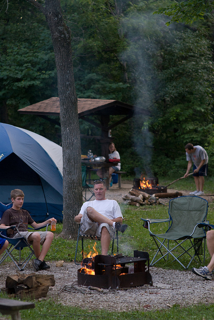 a man and boy sitting in lawn chairs by their campfire