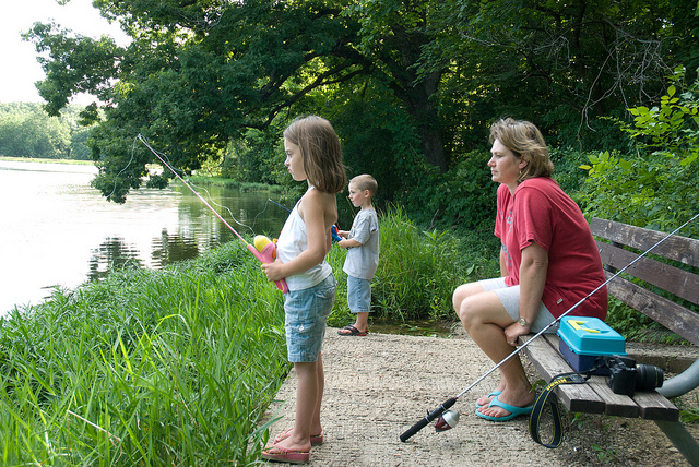two kids fishing off the bank with an adult woman