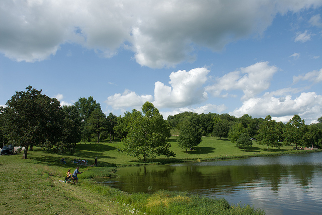 a couple of people sitting on a bench next to the lake on a nice day