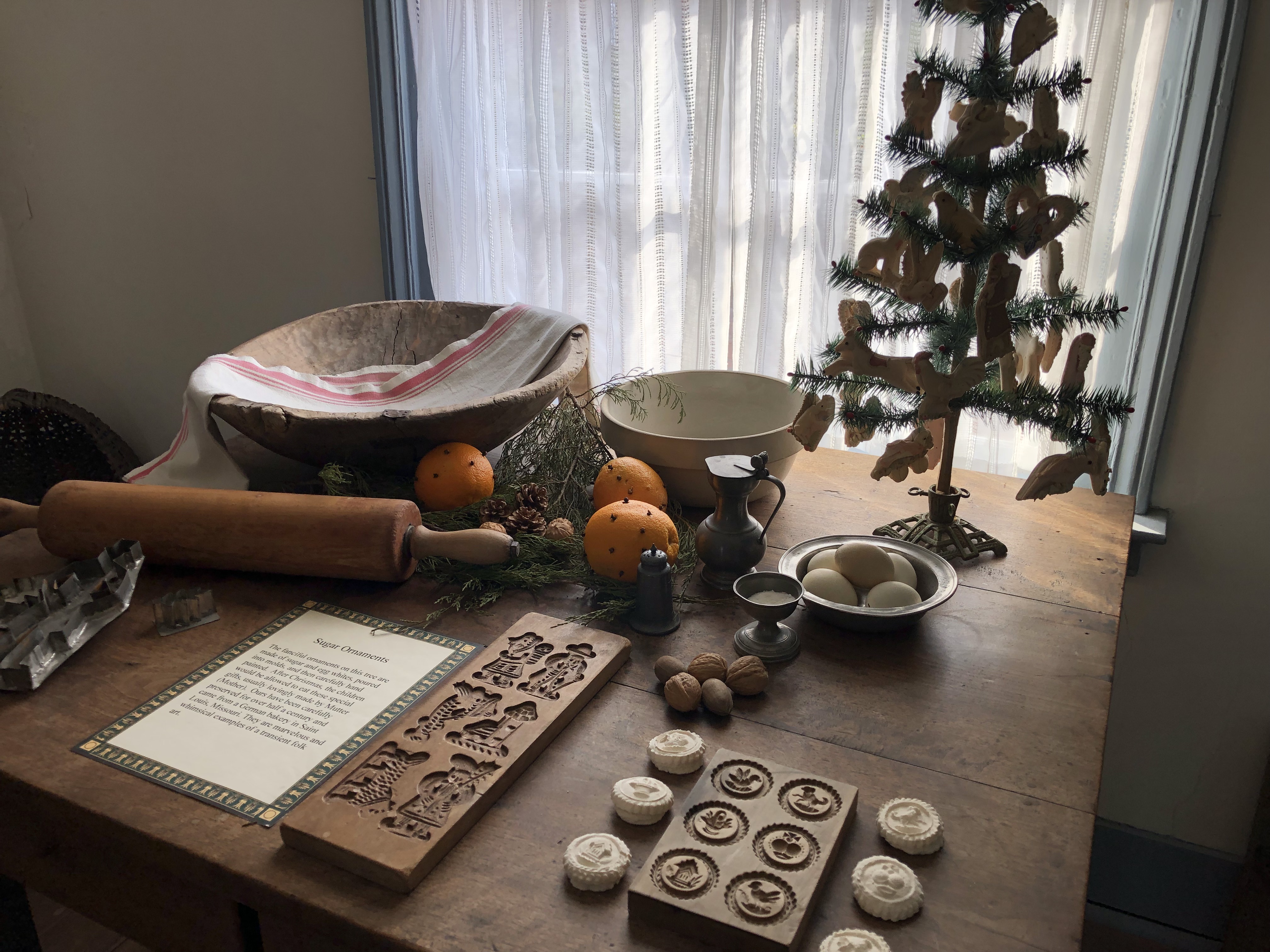 Cookie cutters, springerle mold, rolling pin, bowls, oranges, nuts and small Christmas tree on table