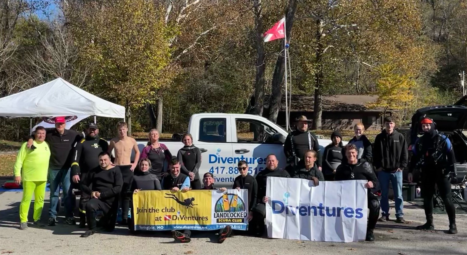 Members of the Diventures diving group pose in front of their white pickup truck and hold up banners for their organization