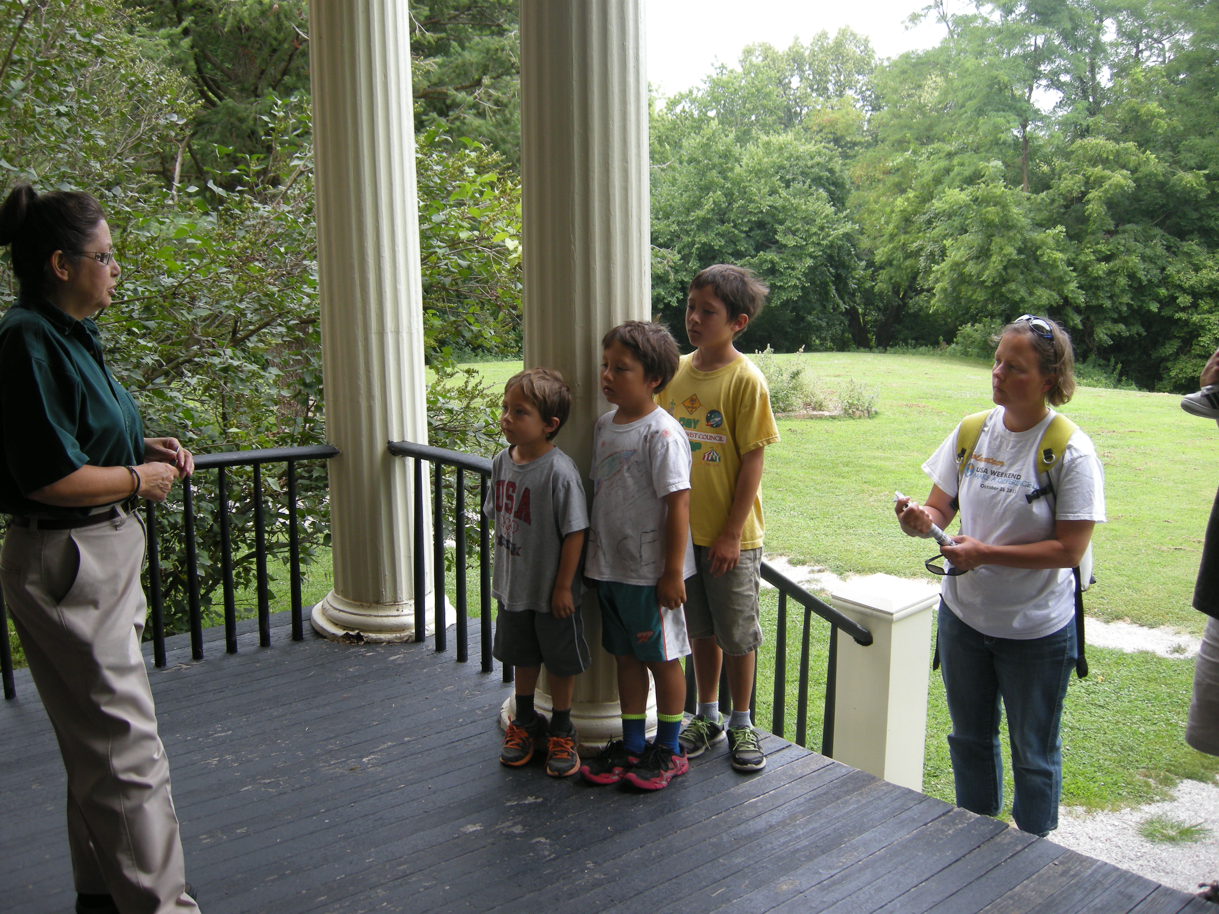 a family stands on the porch of the Anderson House with the tour guide